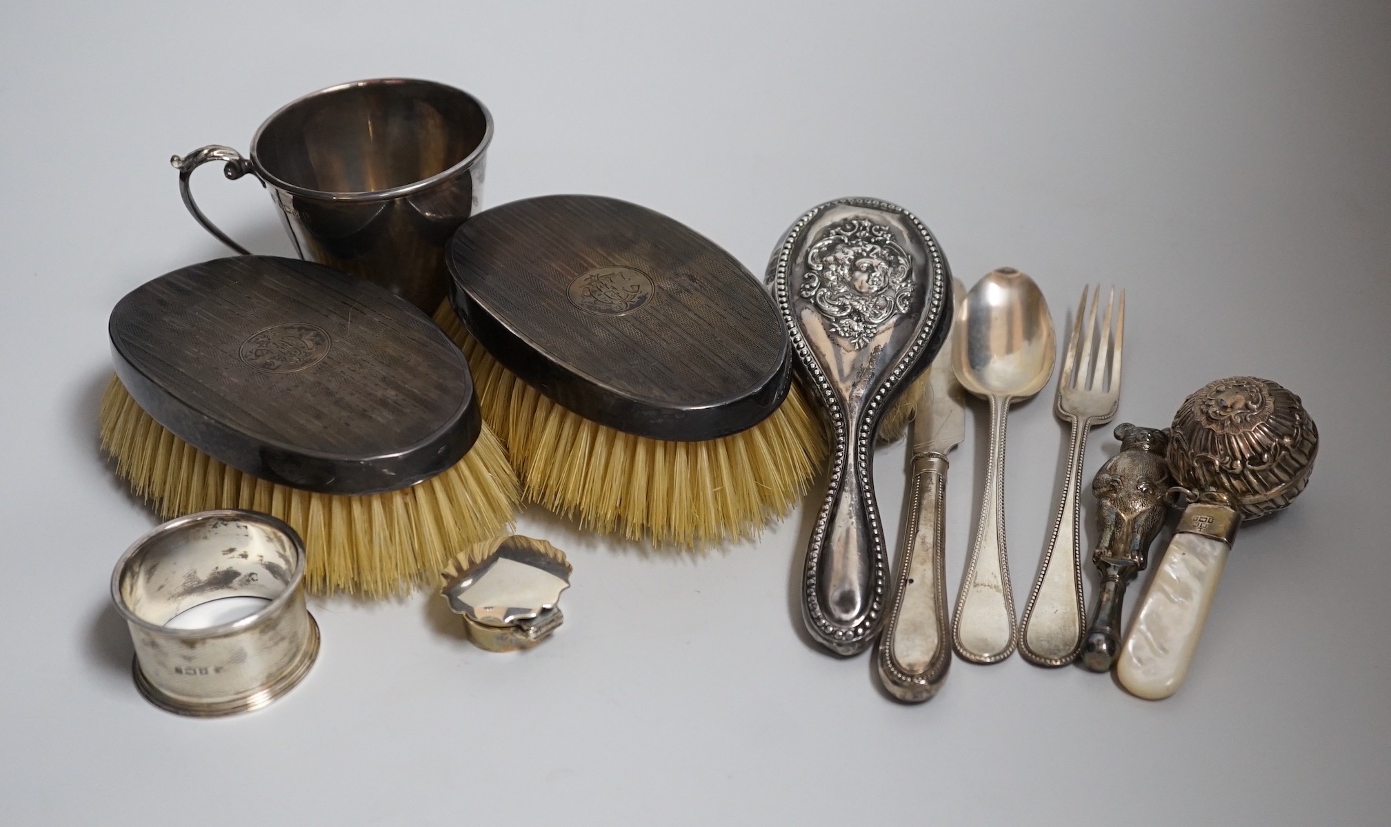 A mixed group of silverware including a pair of silver mounted clothes brushes, two rattles, a napkin ring, a christening trio and mug.